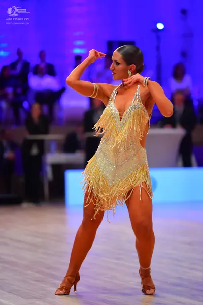 Dancesport competitor: Female dancer: light gold sequined Latin dress with long fringe and an open back