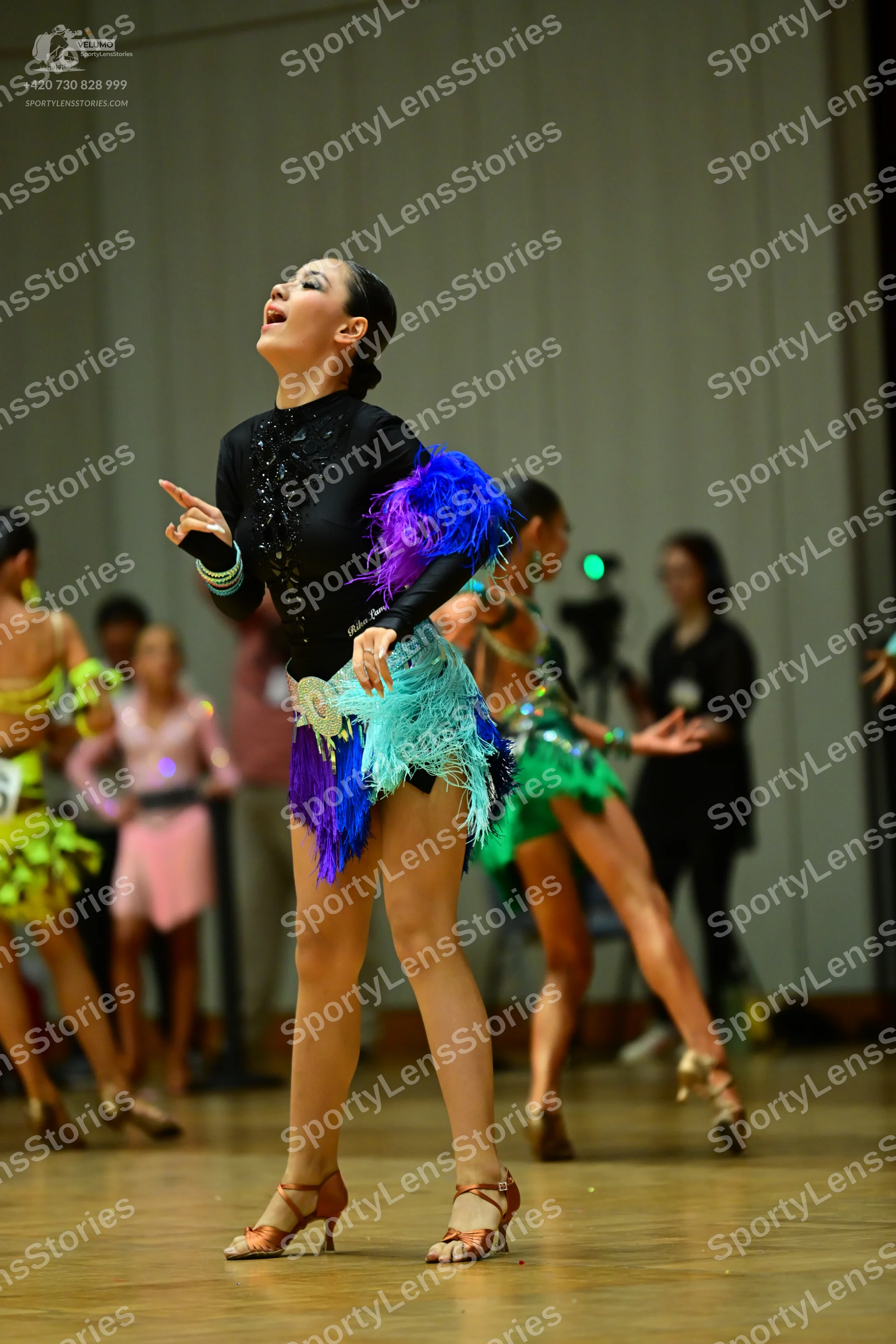 Dancesport competitor: Female dancer (foreground): black long-sleeved top with blue, purple, and teal f