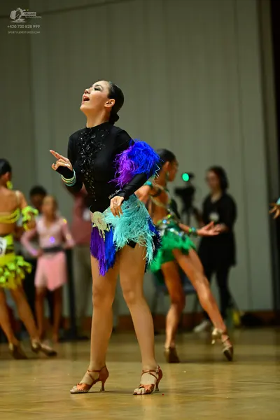 Dancesport competitor: Female dancer (foreground): black long-sleeved top with blue, purple, and teal f