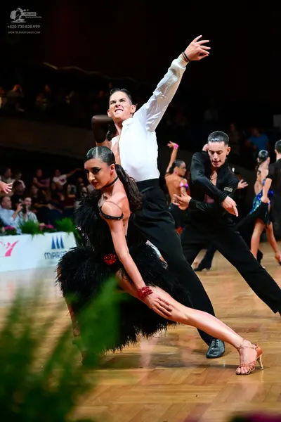 Dancesport competitor: Female dancer in foreground: black Latin dress with feathery texture and a red e
