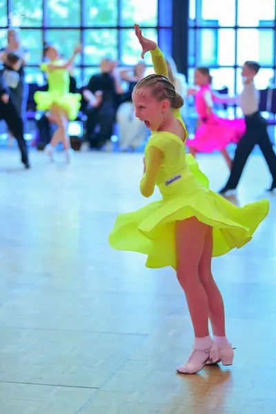 Dancesport competitor: Female dancer in foreground: bright yellow Latin dress with long sleeves and a s