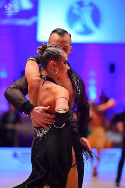 Dancesport competitor: Female dancer: black latin dress with sequins and a high slit, accessorized with