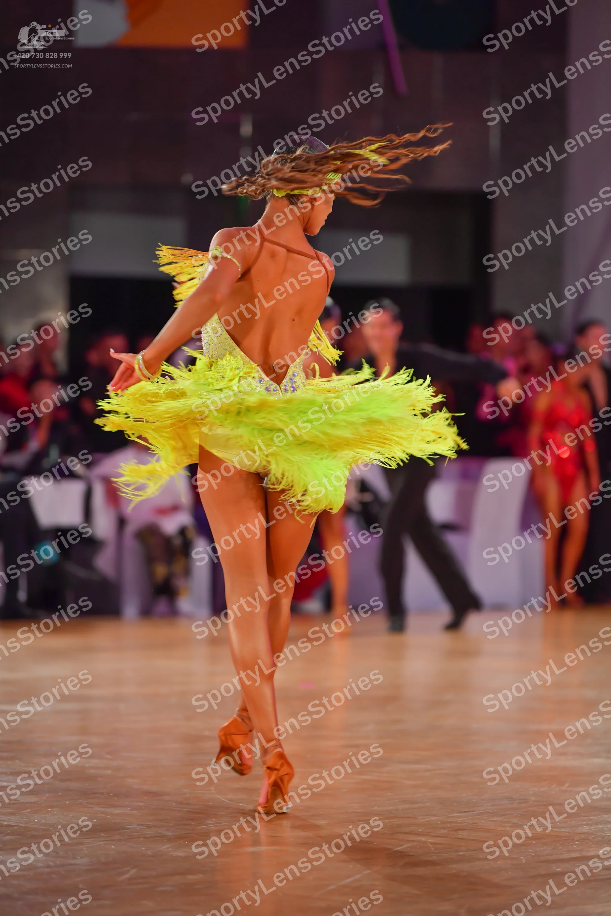 Dancesport competitor: Female dancer (foreground): bright yellow Latin dress with a backless, sequined