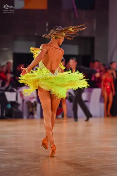 Dancesport competitor: Female dancer (foreground): bright yellow Latin dress with a backless, sequined 