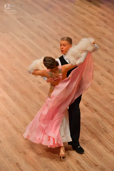 Dancesport competitor: Male dancer: black vest, white long-sleeved shirt with ruffled cuffs, and black 