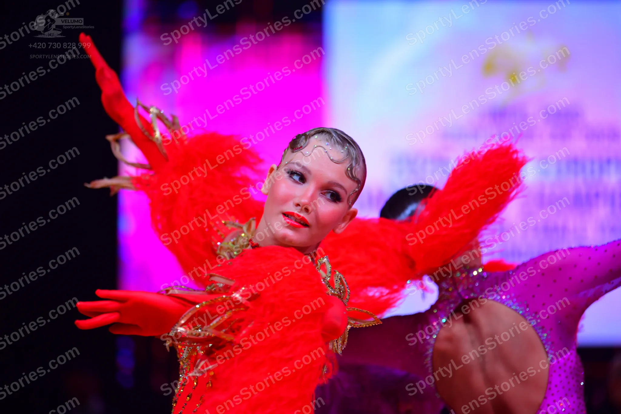 Dancesport competitor: Female dancer 1: red latin dress with gold sequin embellishments and red feather