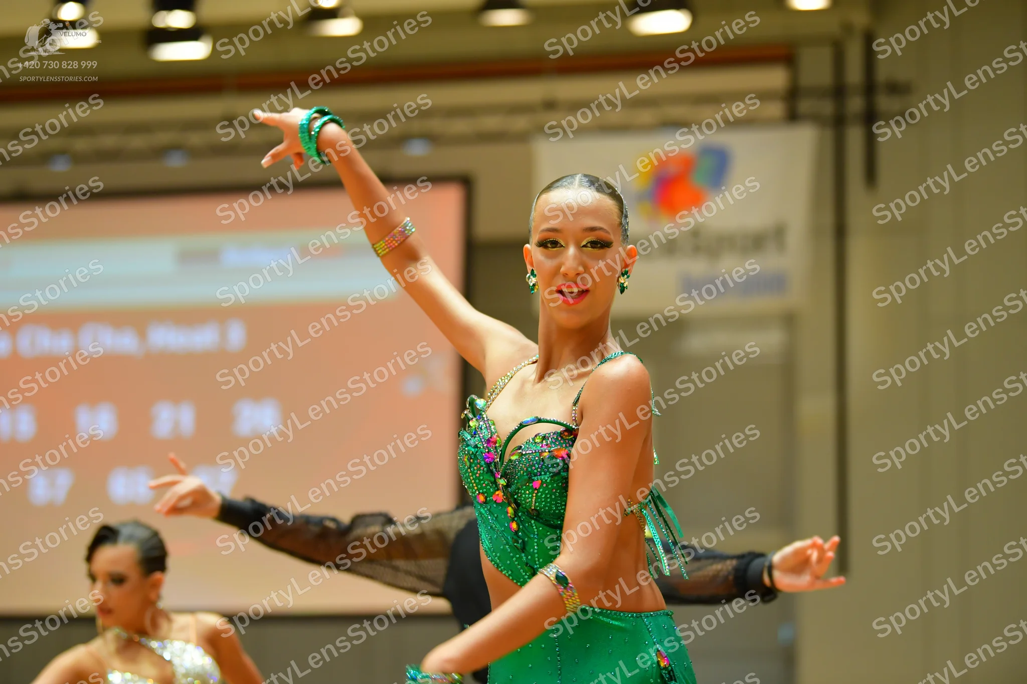 Dancesport competitor: Female dancer in foreground: green sequined Latin dance dress with green bangles