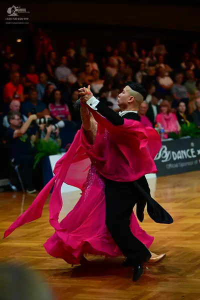 Dancesport competitor: Female dancer: voluminous bright pink ballgown with flowing, sheer fabric