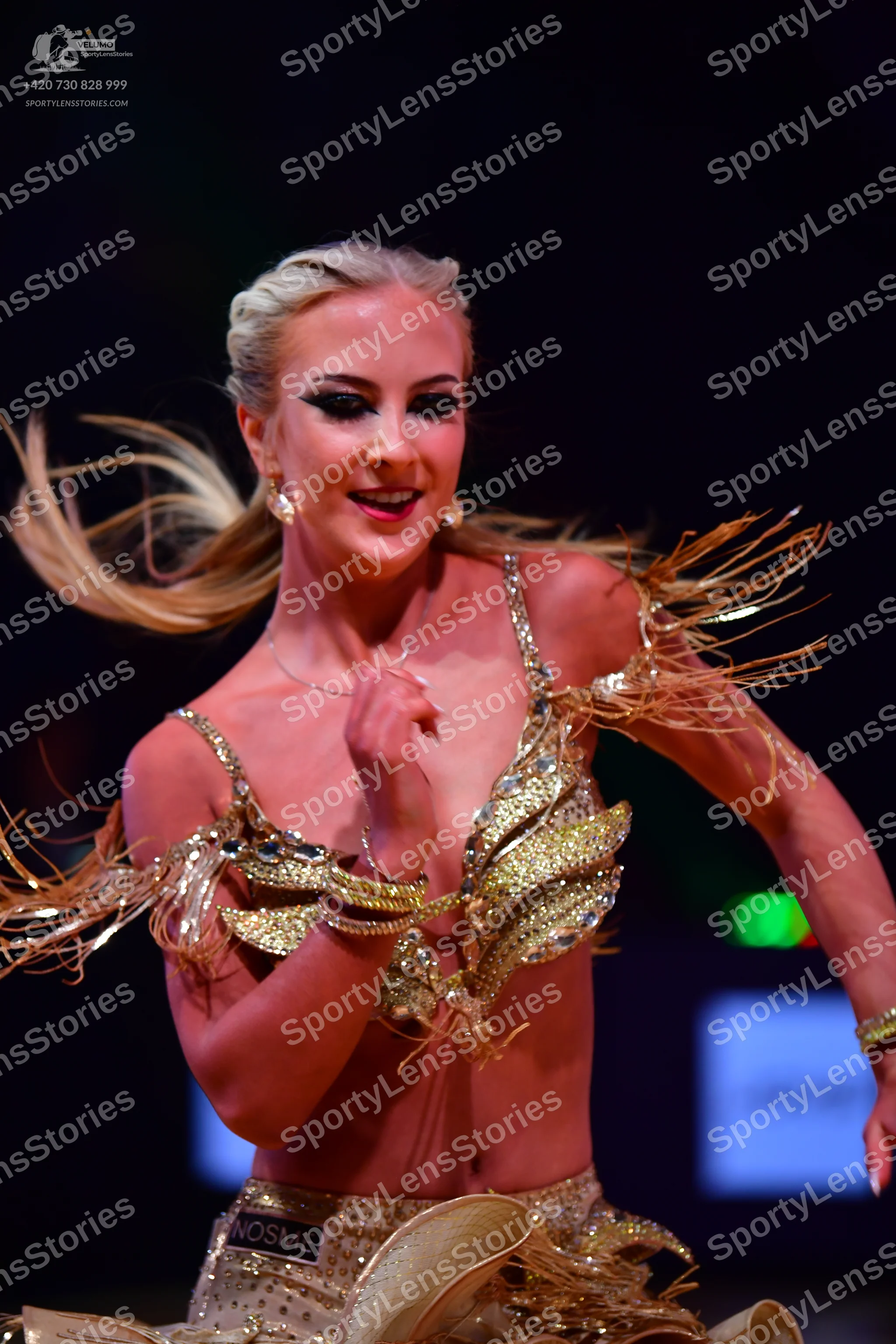 Dancesport competitor: Female dancer: gold sequined Latin dance costume with long, thin, gold-colored s