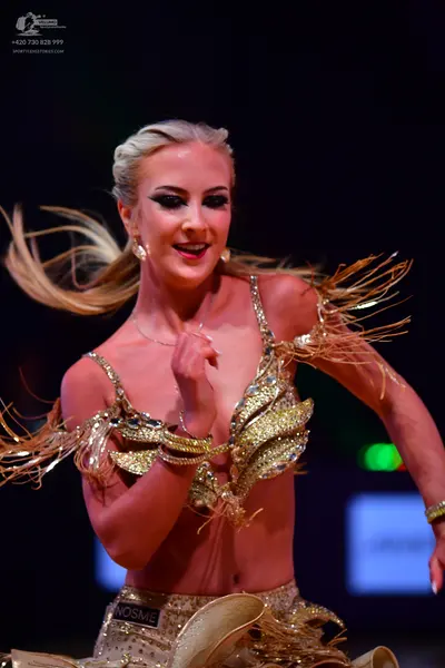 Dancesport competitor: Female dancer: gold sequined Latin dance costume with long, thin, gold-colored s