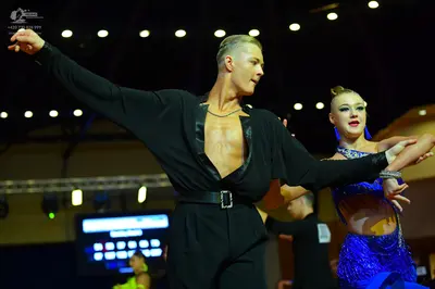 Dancesport competitor: Male dancer: black long-sleeved shirt with a deep neckline and black trousers wi