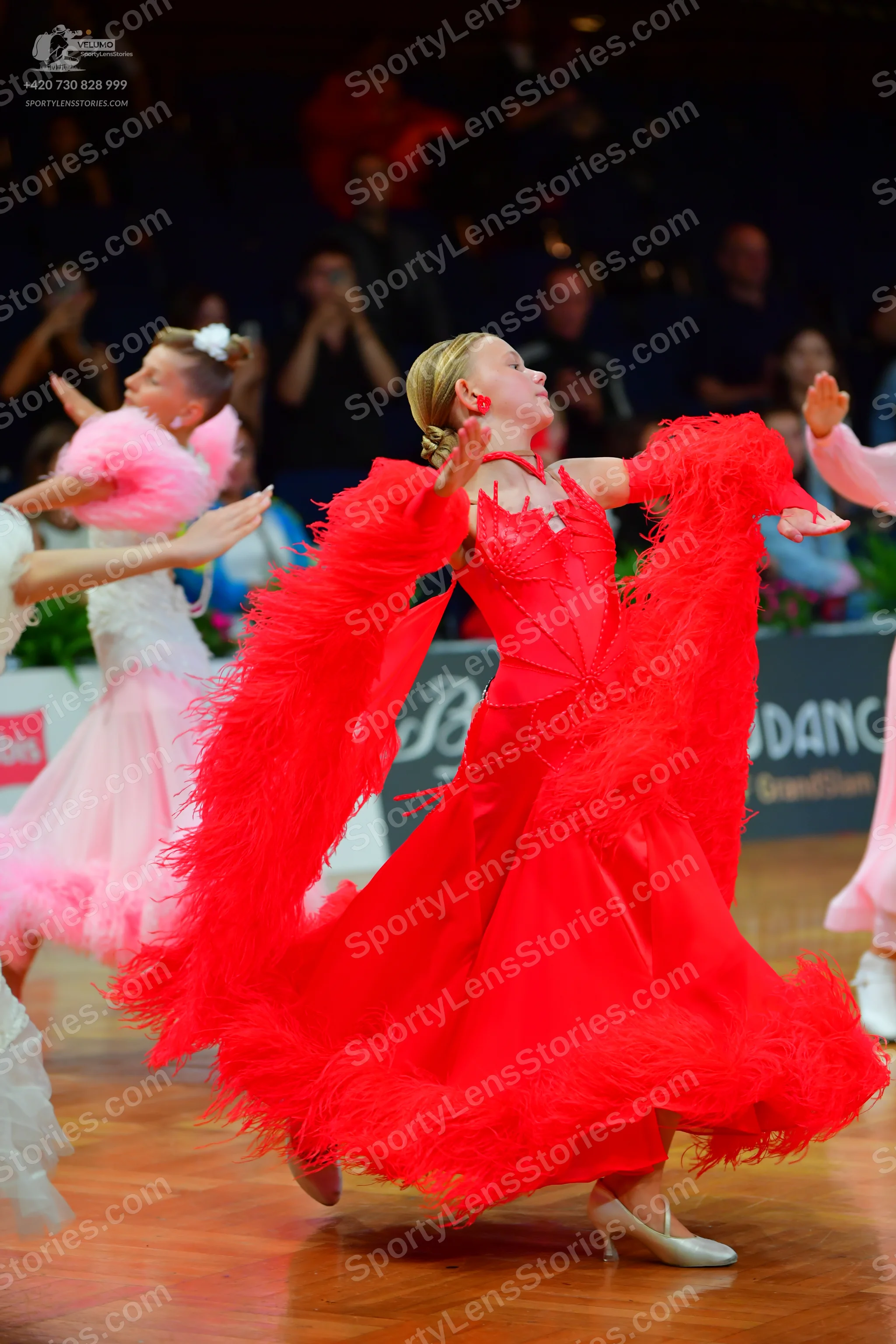 Dancesport competitor: Female dancer in foreground: red ballroom dress with voluminous, feathered sleev