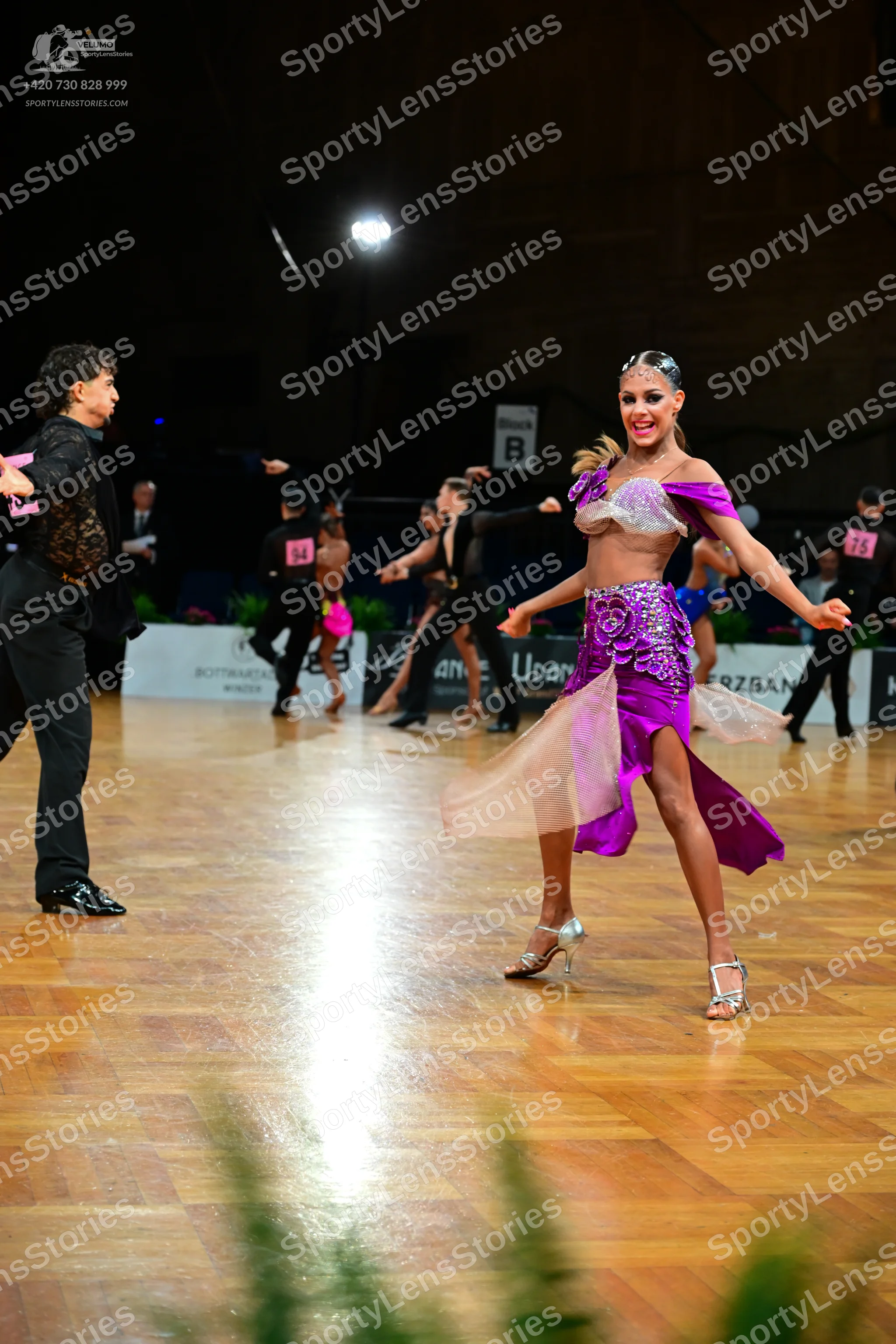Dancesport competitor: Female dancer in foreground: purple/magenta latin dress with a white/silver sequ