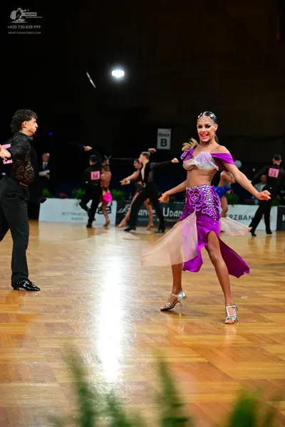 Dancesport competitor: Female dancer in foreground: purple/magenta latin dress with a white/silver sequ