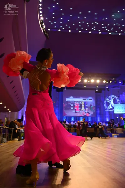 Dancesport competitor: Female dancer: bright pink ballroom dress with large, voluminous, peach-colored 