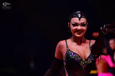 Dancesport competitor: Female dancer (foreground): black Latin dance costume featuring multi-colored rh