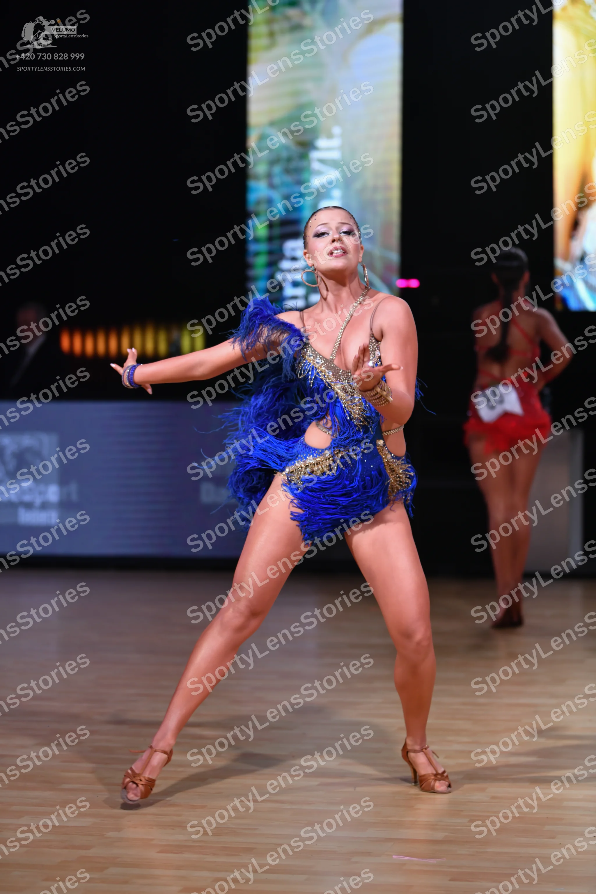 Dancesport competitor: Female dancer in foreground: blue latin dance dress with gold sequins and blue f