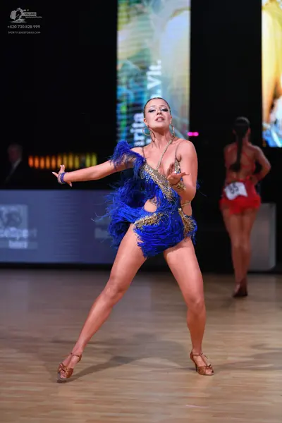 Dancesport competitor: Female dancer in foreground: blue latin dance dress with gold sequins and blue f