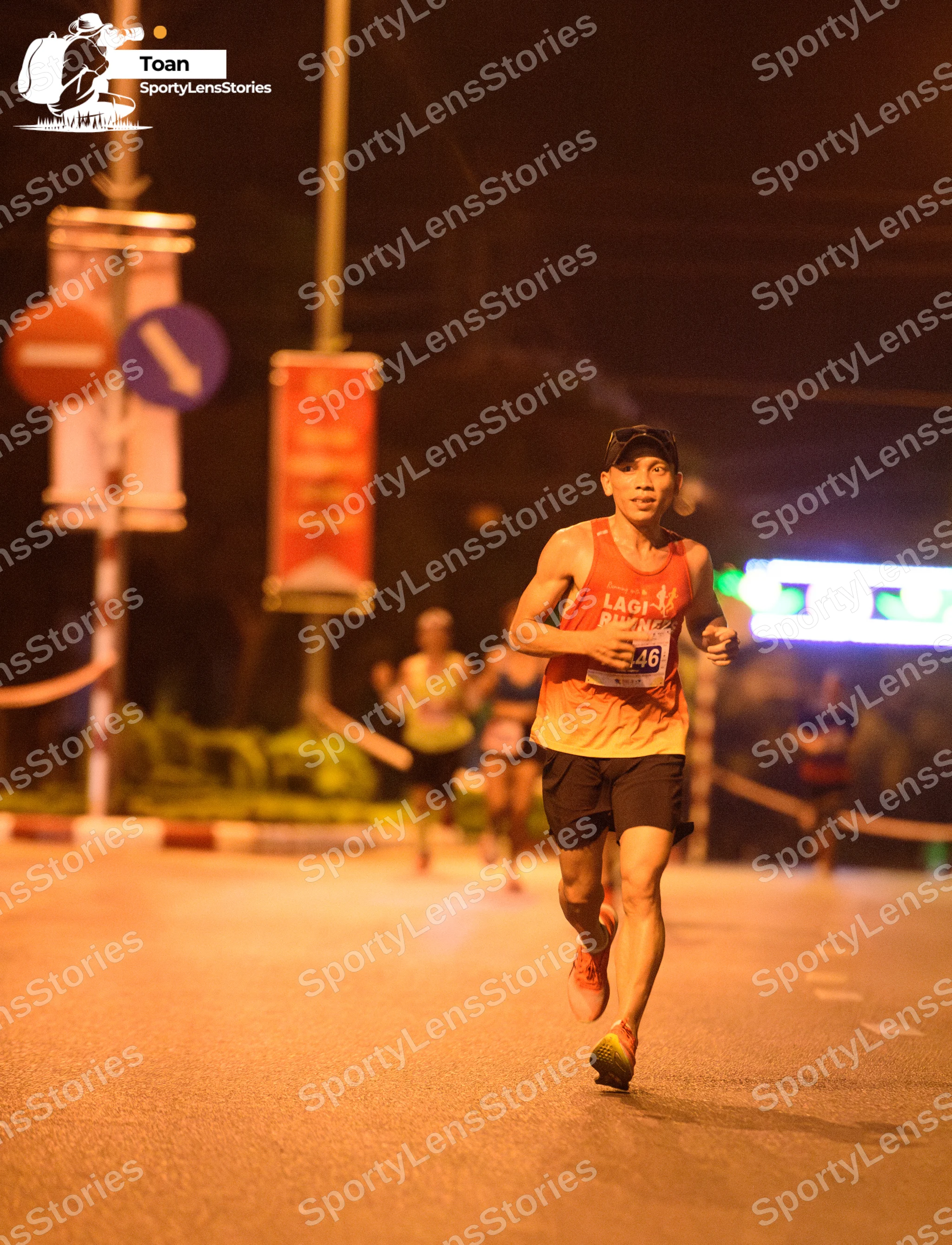 Marathon runner #46: Runner 1: yellow/orange tank top, black shorts, black cap, dark shoes