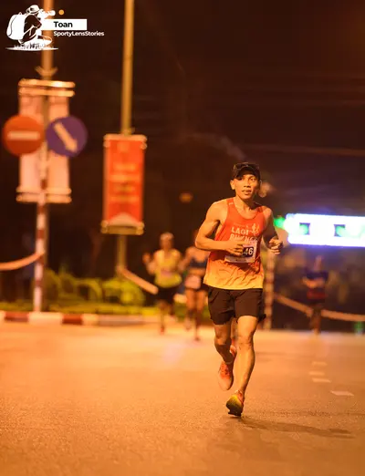 Marathon runner #46: Runner 1: yellow/orange tank top, black shorts, black cap, dark shoes