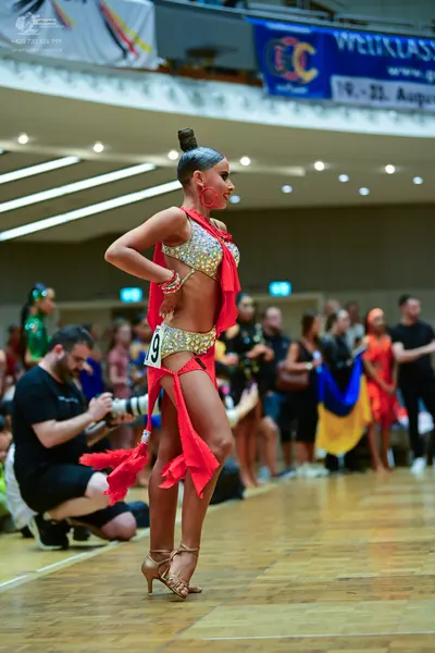 Dancesport competitor: Female dancer: gold and silver sequined latin dance two-piece with red fabric dr