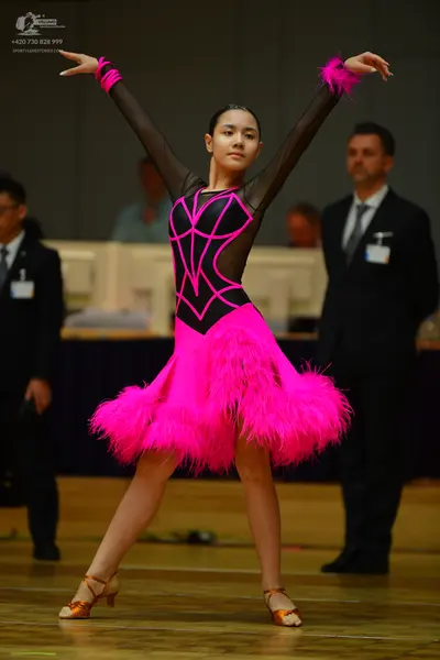 Dancesport competitor: Female dancer: pink and black Latin dress with a feather skirt and feather cuffs