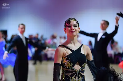 Dancesport competitor: Female dancer in center: black latin dress with gold sequin embroidery and cutou