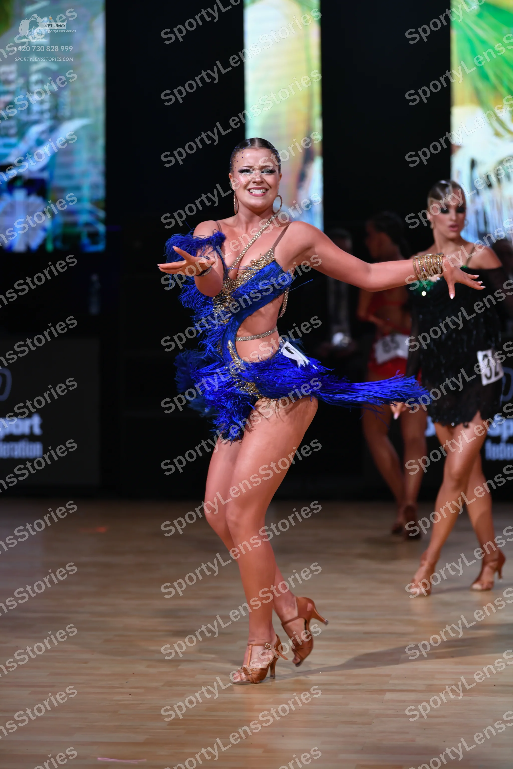 Dancesport competitor: Female dancer in front: blue Latin dance dress featuring blue feathers and gold