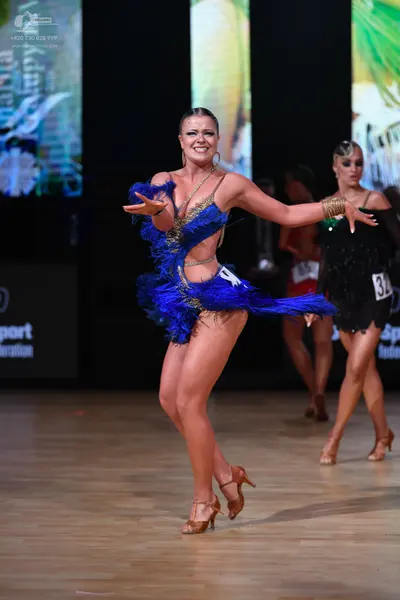 Dancesport competitor: Female dancer in front: blue Latin dance dress featuring blue feathers and gold 