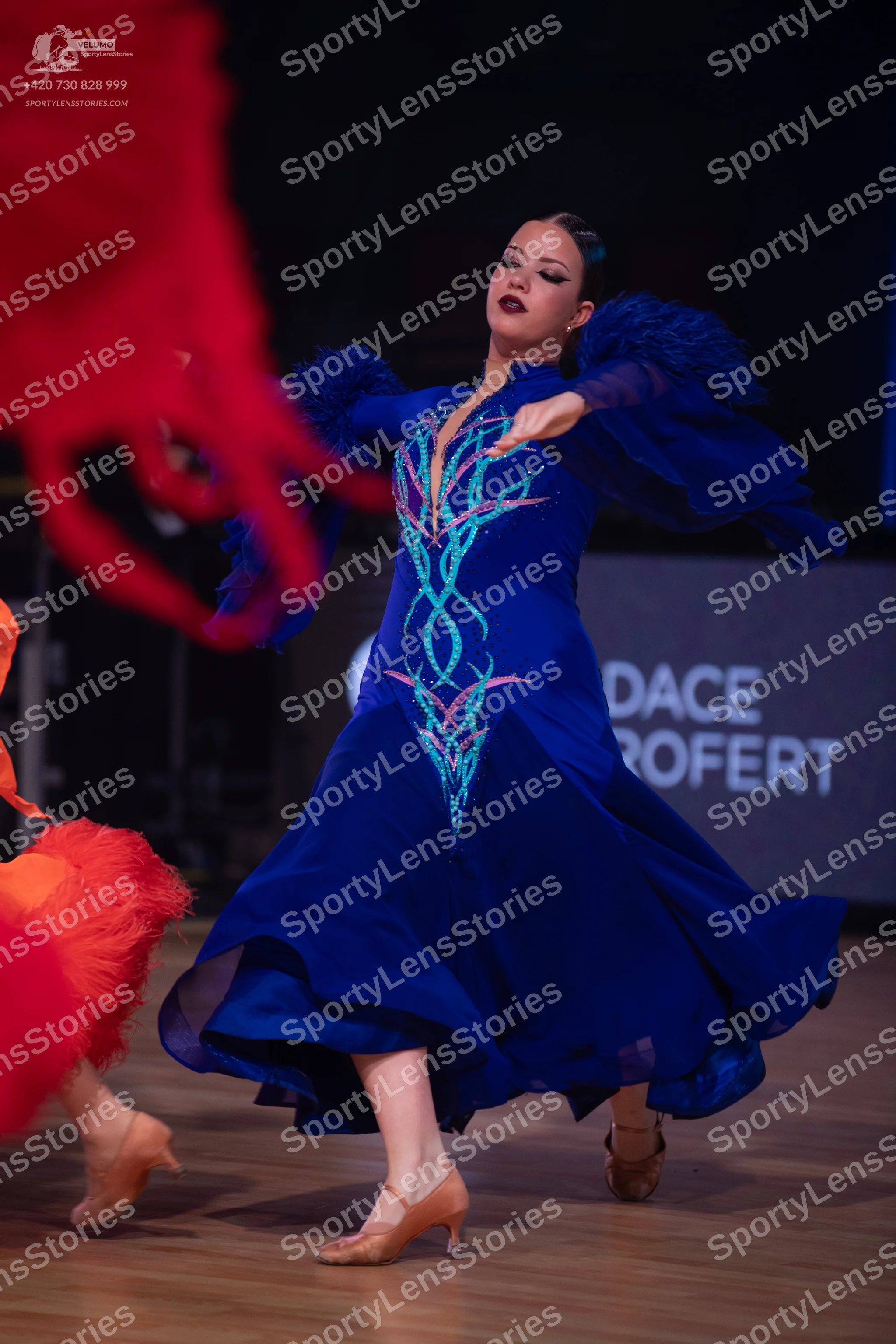 Dancesport competitor: Female dancer in center: royal blue ballroom dress with voluminous, ruffled slee