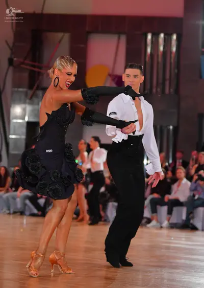 Dancesport competitor: Female dancer: black short Latin dress with large 3D floral embellishments, long