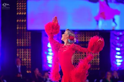 Dancesport competitor: Female dancer: red Latin dress with red feather/fringe accents on the sleeves an
