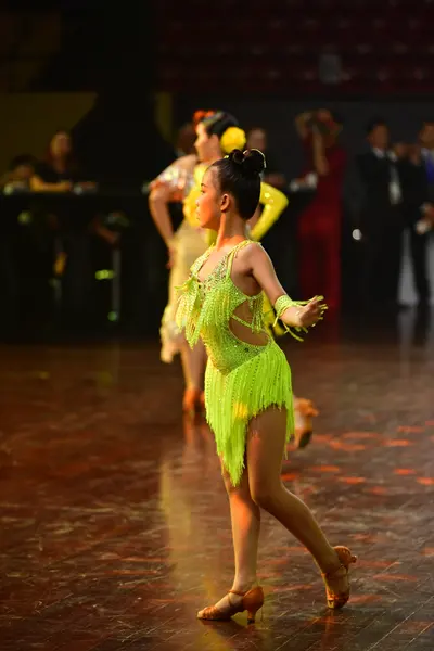 Dancesport competitor: Female dancer in foreground: lime green Latin dance dress with fringe and cut-ou