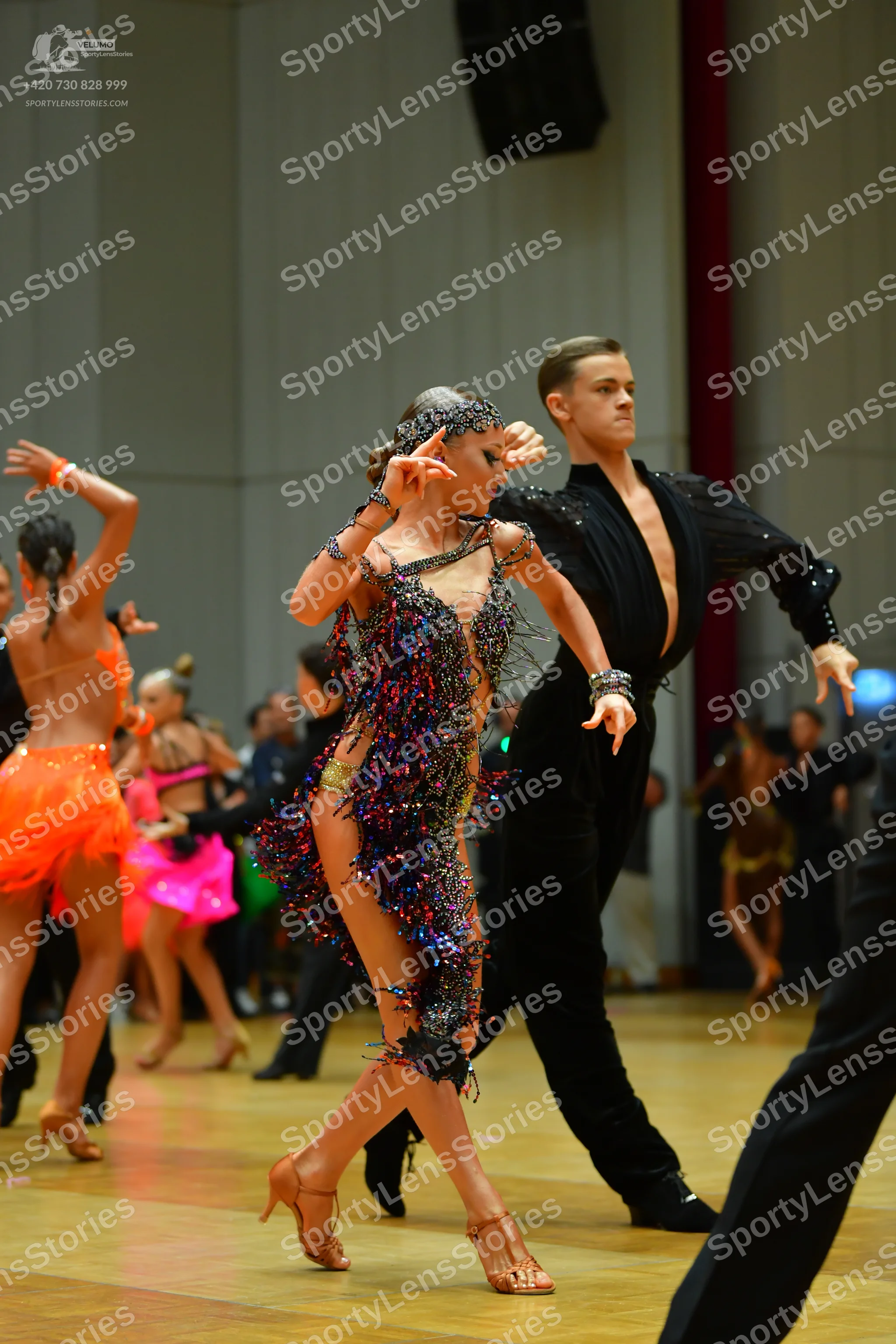 Dancesport competitor: Female dancer in center: multicolored (blue, purple, pink, gold) sequined and fr