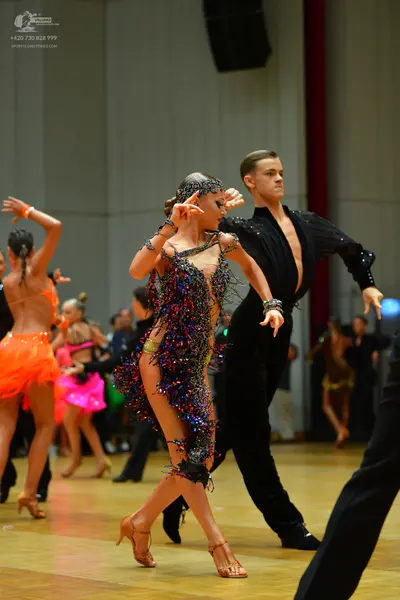 Dancesport competitor: Female dancer in center: multicolored (blue, purple, pink, gold) sequined and fr