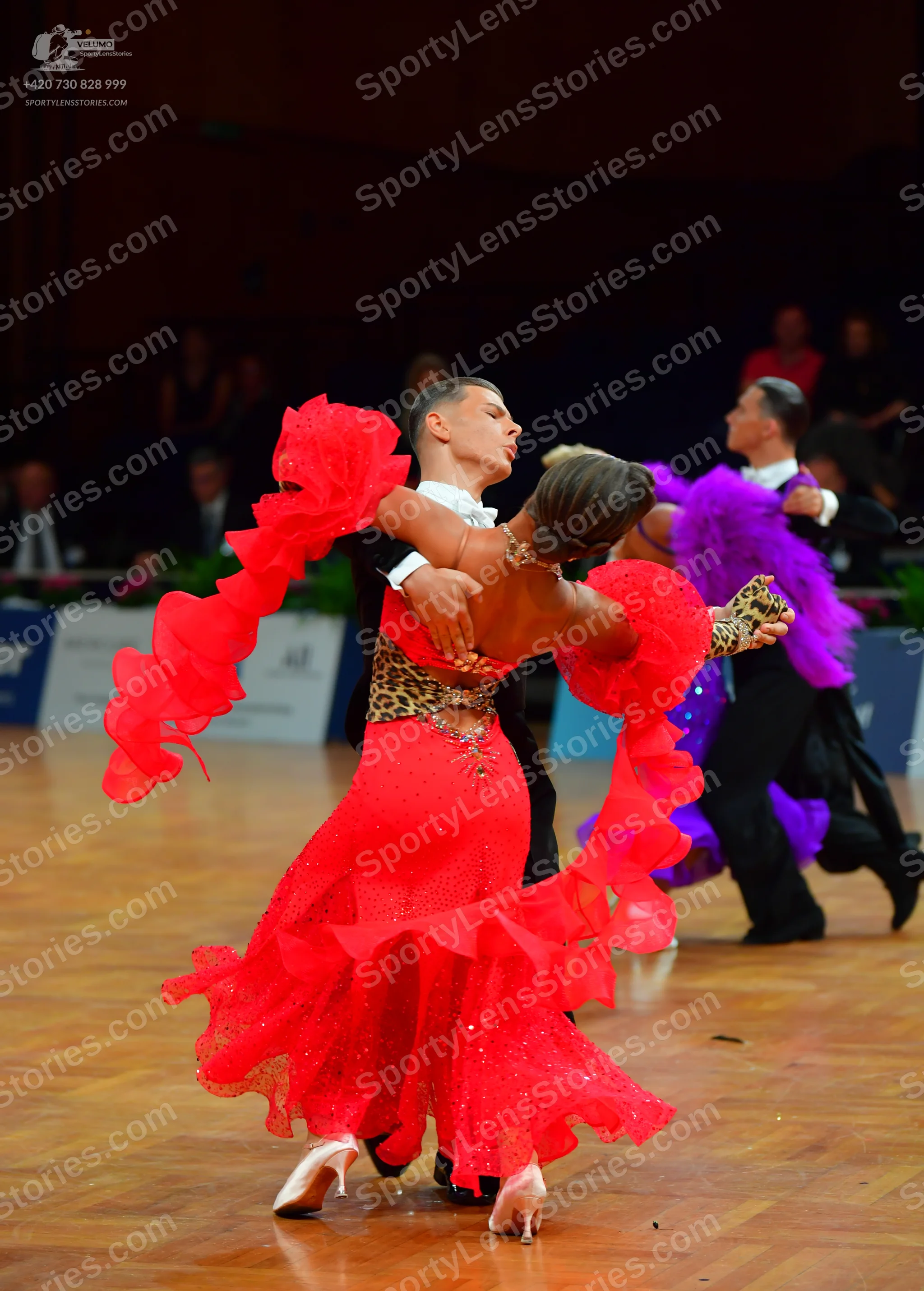 Dancesport competitor: Female dancer (foreground): red Latin dress with a leopard print bodice and larg