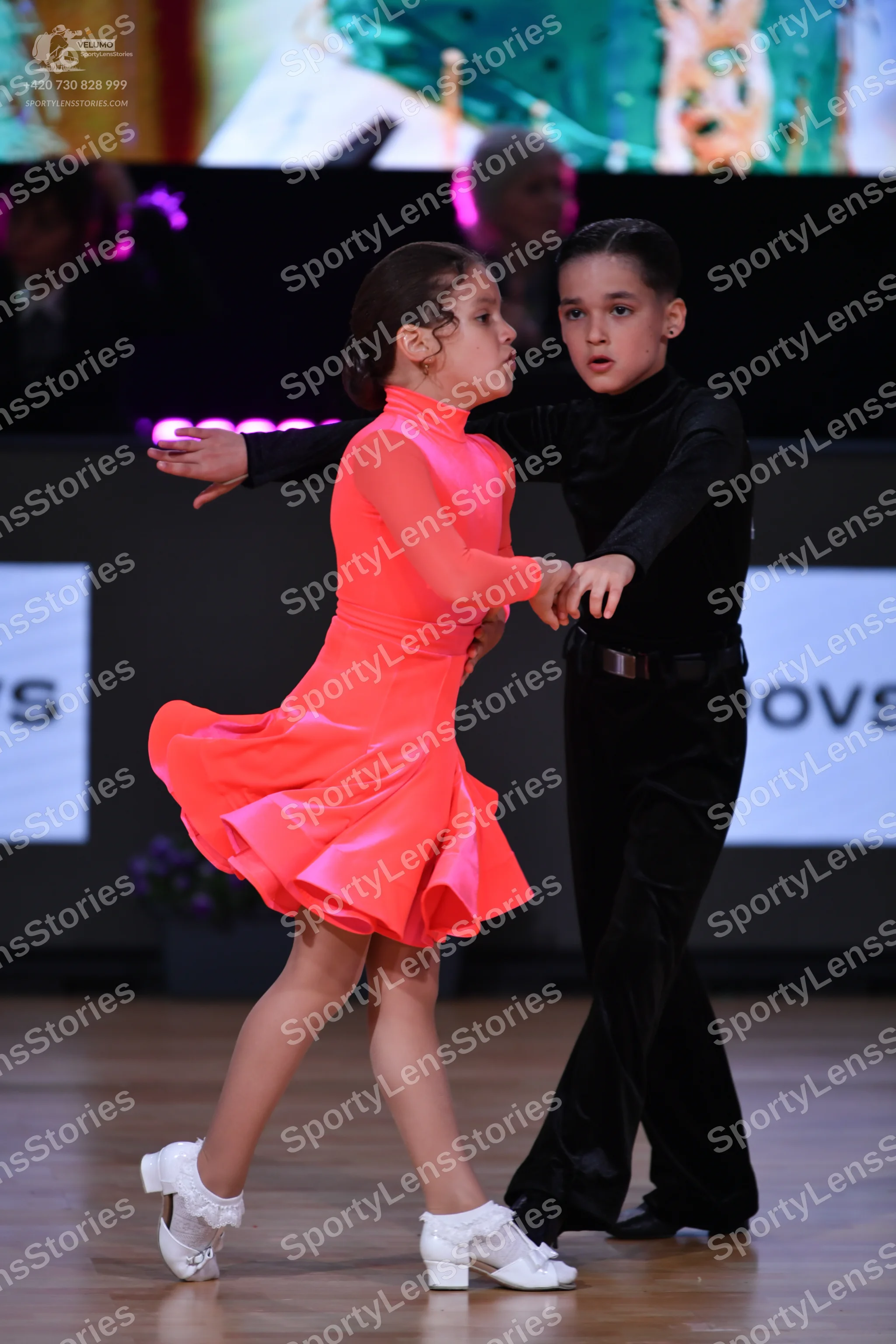 Dancesport competitor: Female dancer: bright coral long-sleeved Latin dance dress with a high neck and