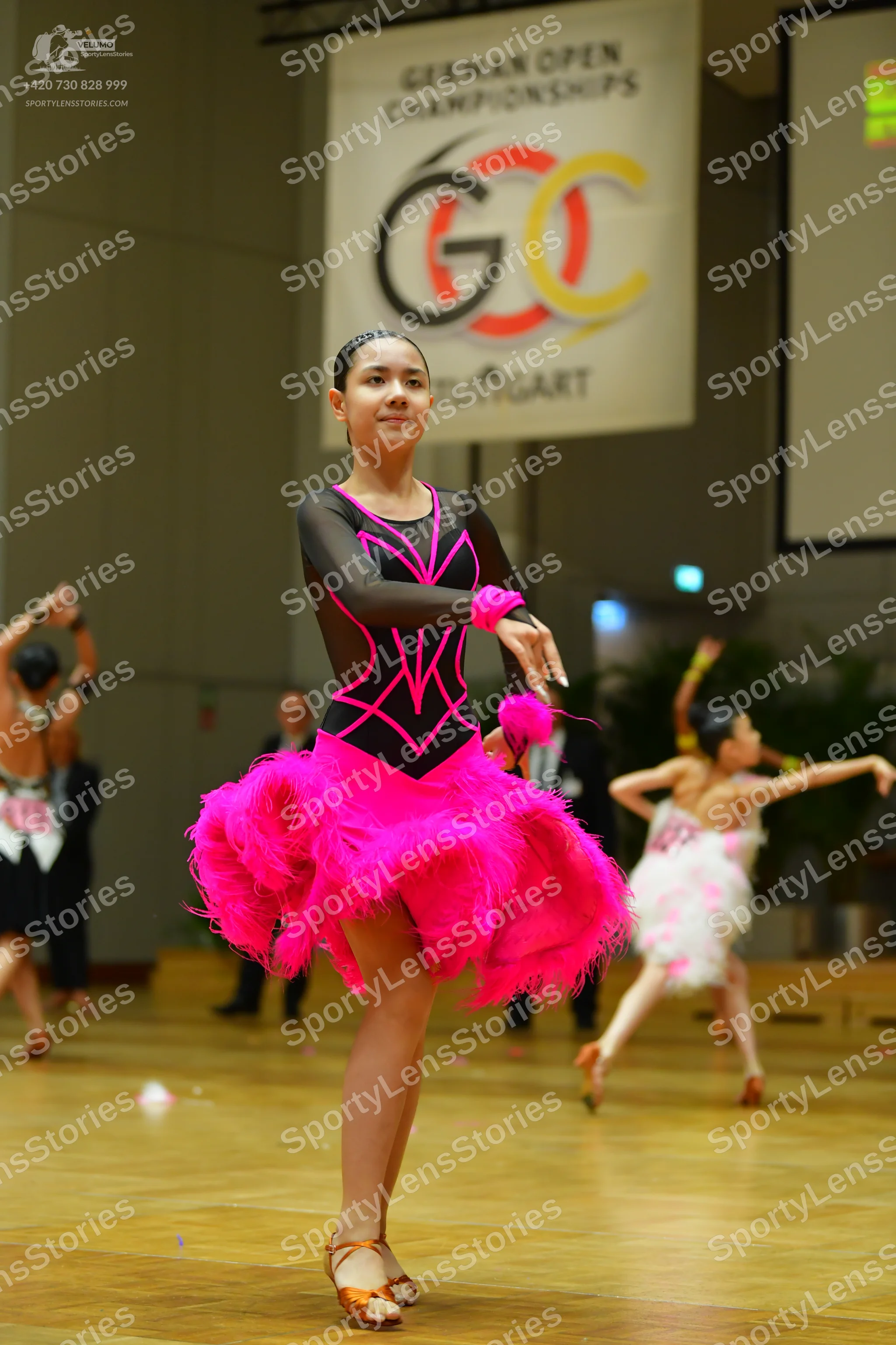 Dancesport competitor: Female dancer in foreground: black Latin dance dress with bright pink trim and a