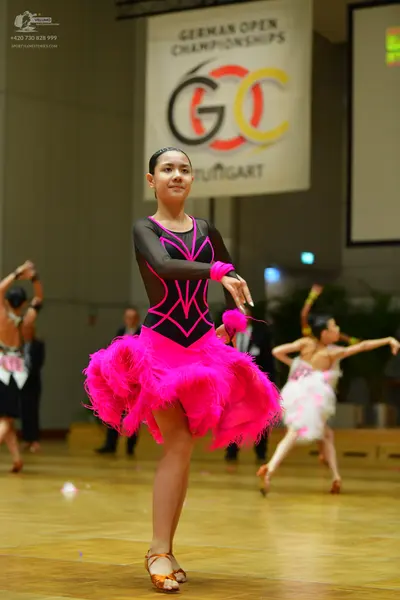 Dancesport competitor: Female dancer in foreground: black Latin dance dress with bright pink trim and a