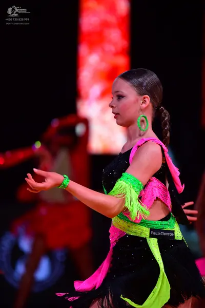 Dancesport competitor: Female dancer: black Latin dress with neon green and bright pink fringe and fabr