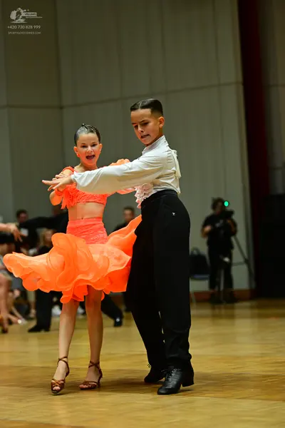 Dancesport competitor: Female dancer: bright orange two-piece Latin costume with a ruffled, layered ski