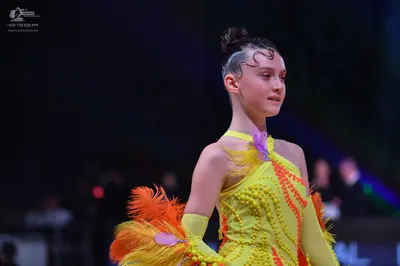 Dancesport competitor: Female dancer: bright yellow latin dress with orange and yellow feathers