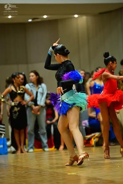 Dancesport competitor: Female dancer in center: black long-sleeved top with purple, blue, turquoise, an
