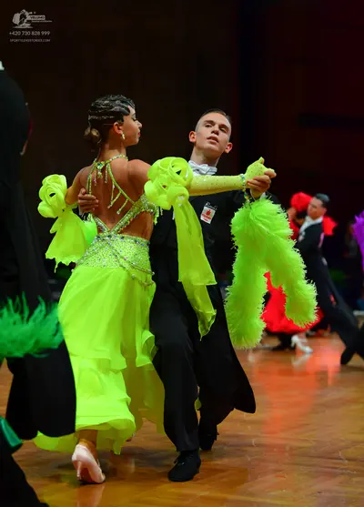 Dancesport competitor: Foreground female dancer: neon green Latin dress with sequins, ruffles, and a lo