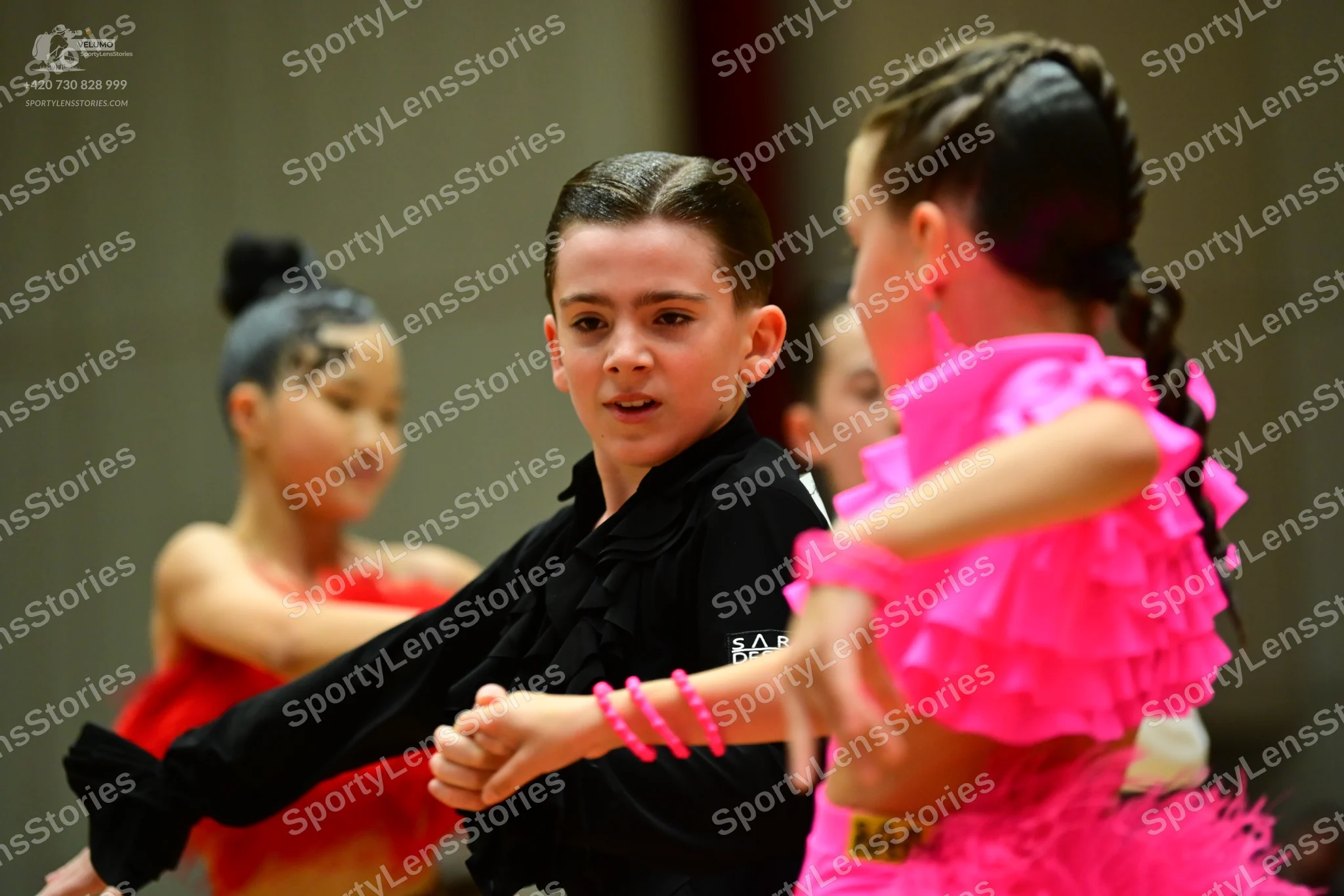 Dancesport competitor: Female dancer (foreground right): bright pink ruffled Latin dress with multiple 