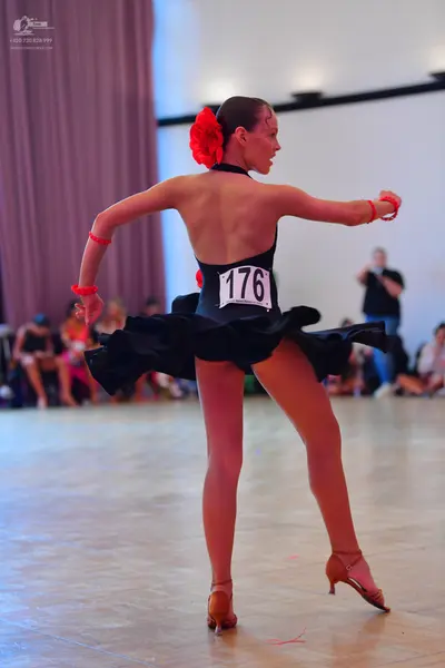 Dancesport competitor #176: Female dancer: black latin dress with a flared skirt, red flower in hair, and re