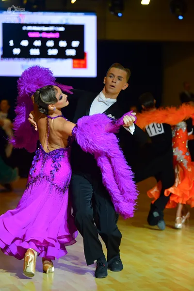 Dancesport competitor #119: Female dancer: magenta Latin dress with sequins, lace, and fringe, accompanied b