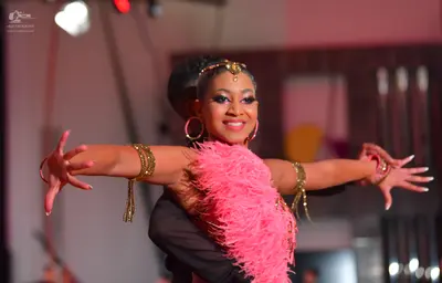 Dancesport competitor: Female dancer: black costume with voluminous pink feather detailing around the n