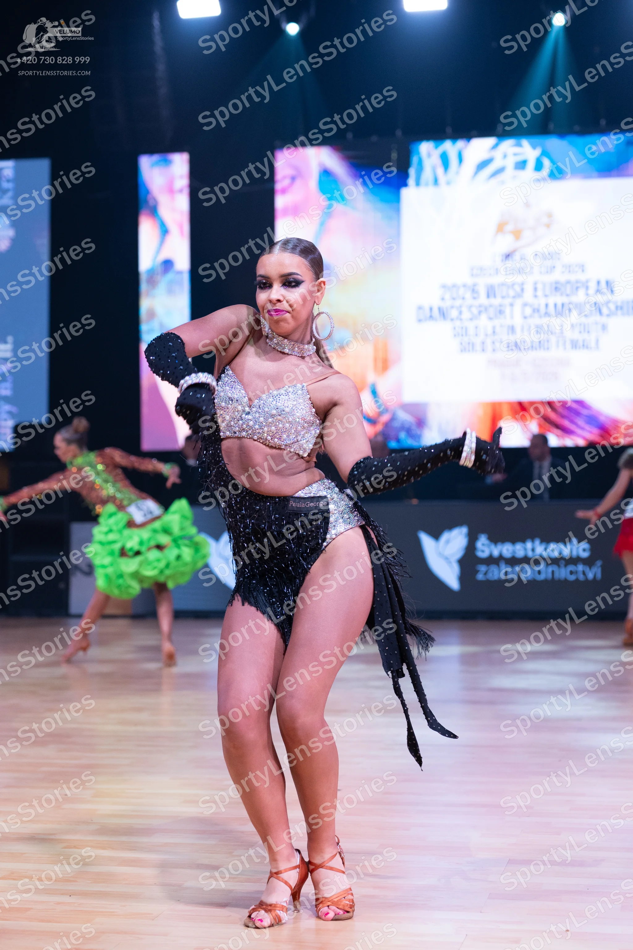 Dancesport competitor: Female dancer (foreground): silver sequin crop top, black sequin and fringe Lati