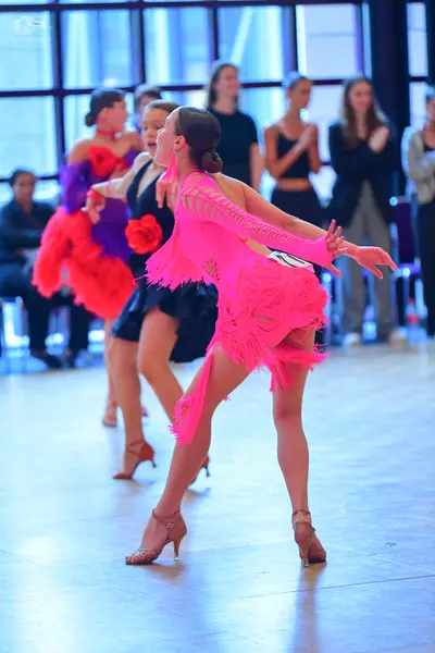 Dancesport competitor: Dancer in foreground: bright pink Latin dance dress with long, flowing fringe on